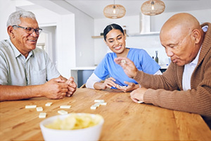 two elderly gentlemen and a caregiver playing games at a table