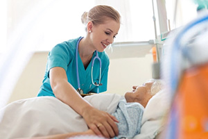 a caregiver wearing blue scrubs helping an elderly woman in her bed