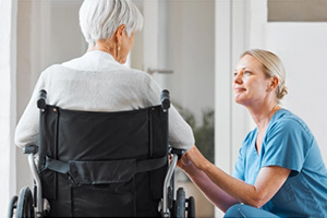 elderly woman in wheelchair speaking with a nurse in blue scrubs