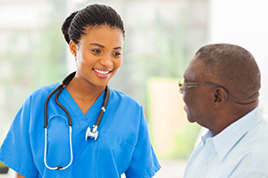smiling nurse in blue scrubs speaking with an elderly patient