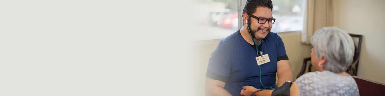 A caregiver wearing blue scrubs checking the pulse of a resident at the Redlands Healthcare Center
