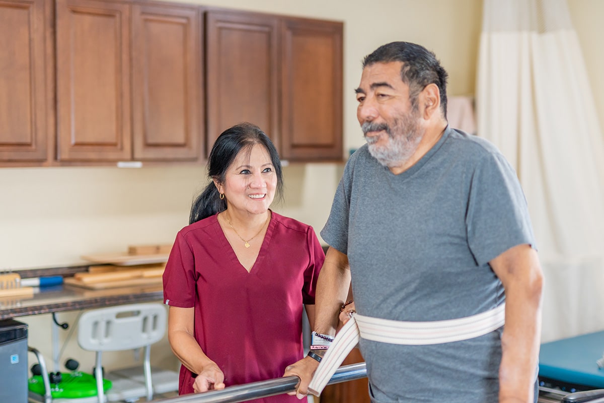 A physical therapist helping a man walk at Redlands Healthcare Center