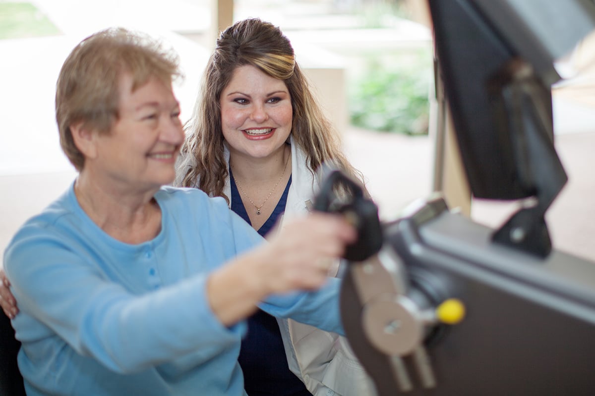 An elderly woman doing an exercise with an employee at Redlands Healthcare Center